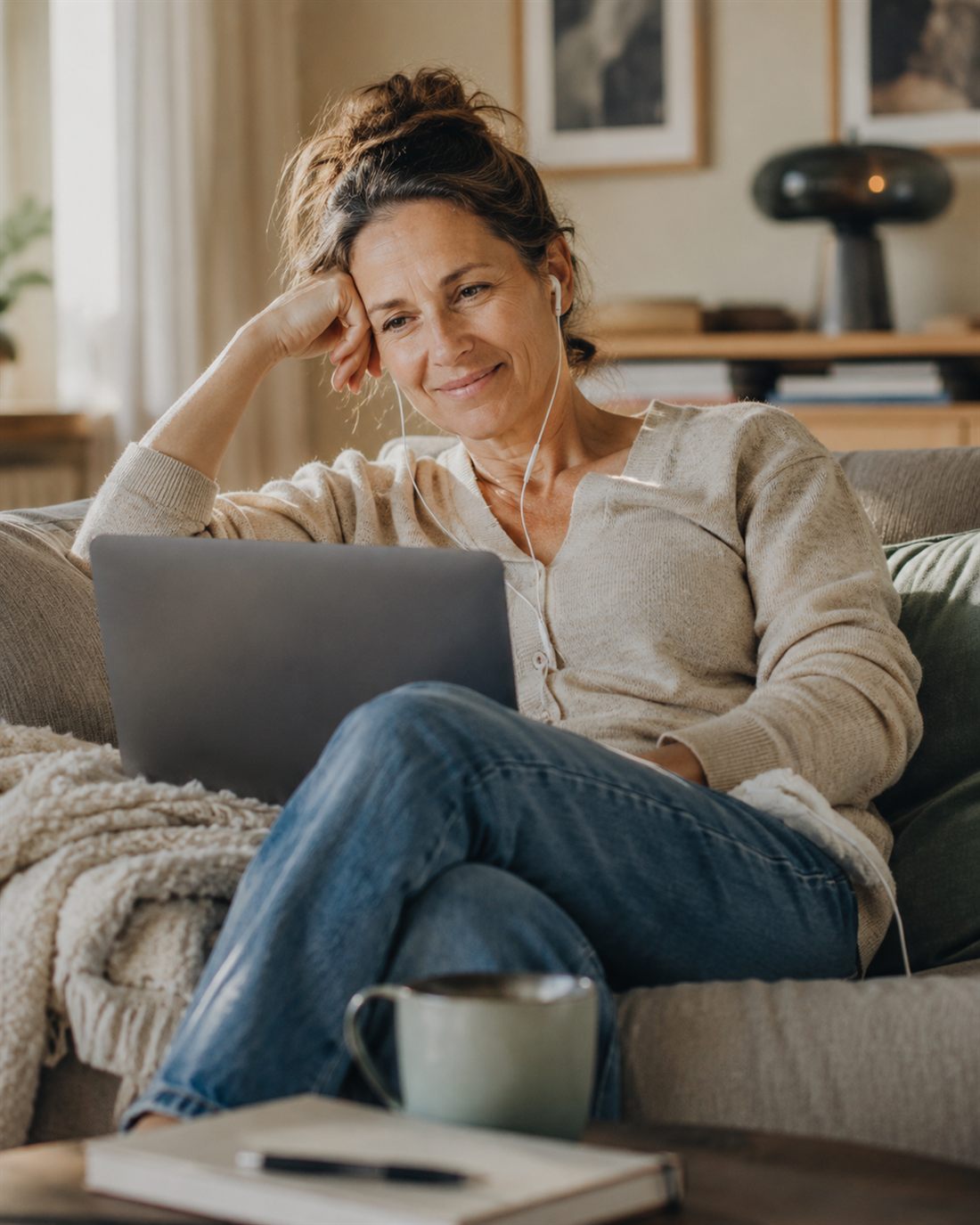 Kvinna sitter i soffan hemma med laptop och hörlurar